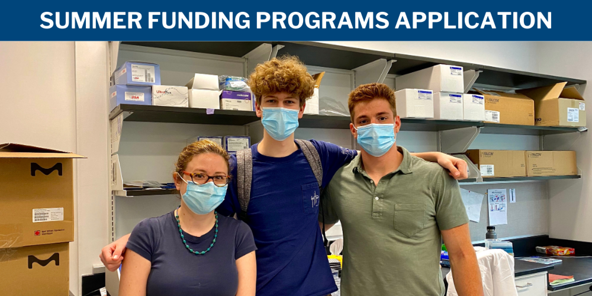 Three people stand in a lab wearing blue masks